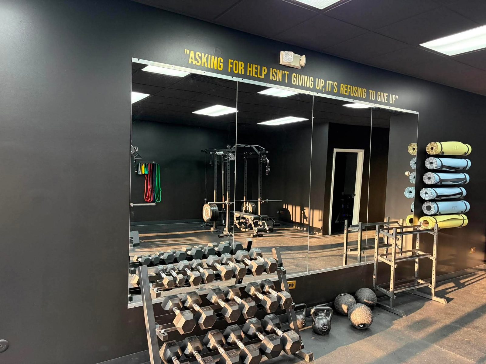 Mirrored wall with motivational quote and dumbbell rack at Odyssey Strength & Recovery